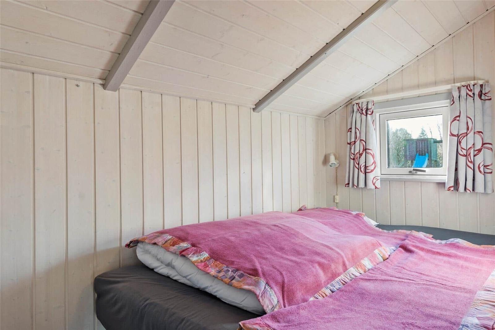 Zwei Liegestühle mit rosa Decken stehen auf einer Holterrasse. Im Hintergrund sind Bäume und ein Haus zu sehen.