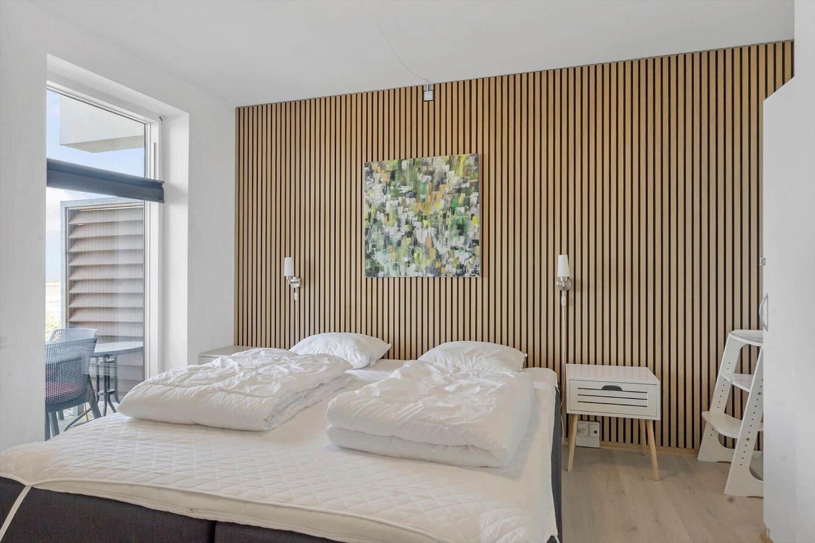 Wohnzimmer mit Sofa, Fernseher und Kamin. Küche im Hintergrund. Holzfußboden und schwarze Ledermöbel.