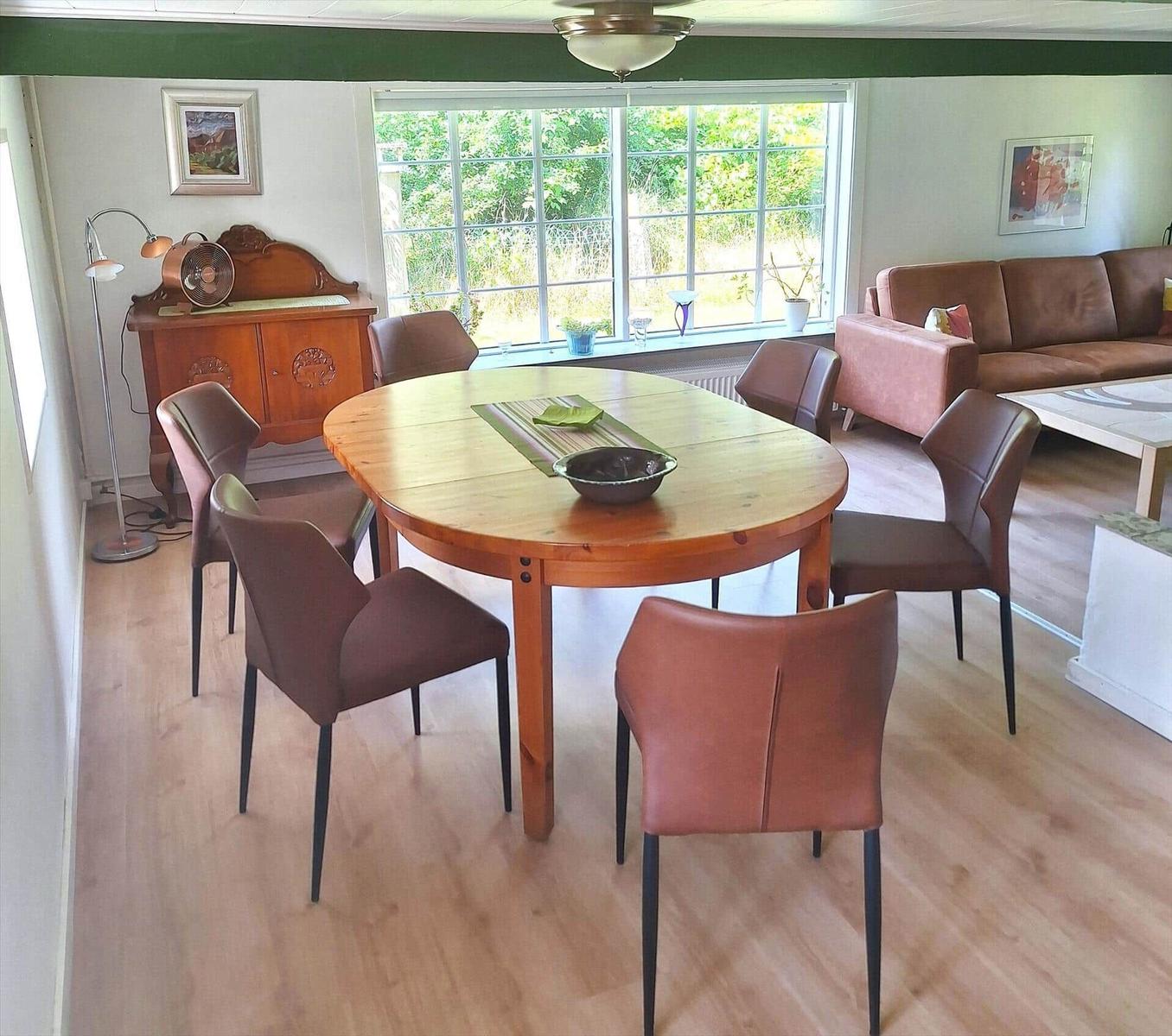 Esszimmer mit Holztisch, Stühlen und Fensterblick auf Grün.