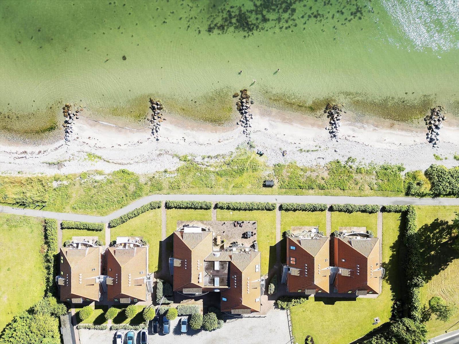 Aerial view of beachfront houses with red roofs and parking area near shoreline.