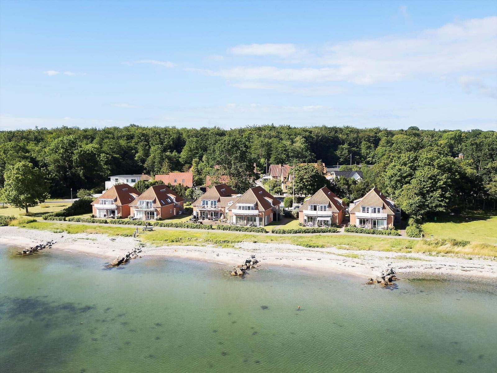 Aerial view of holiday homes near the beach with green areas and water.
