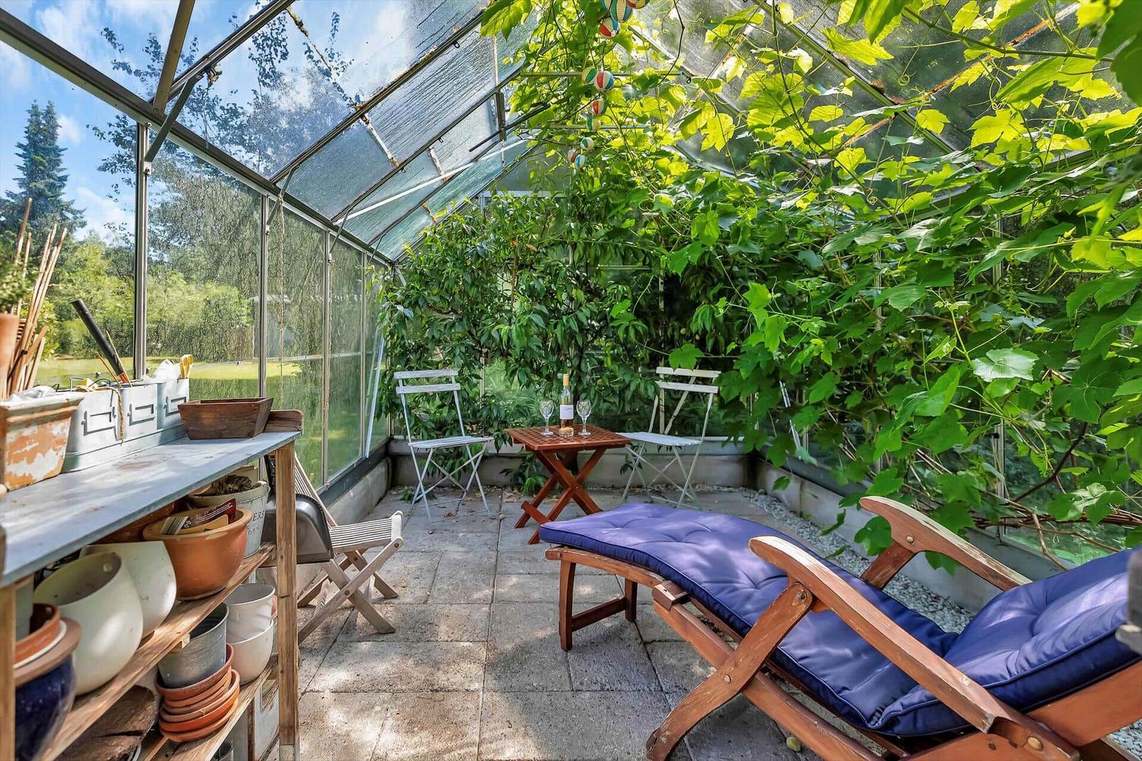 Zwei gestreifte Liegestühle stehen im Garten. Im Hintergrund sind ein Gewächshaus und ein Holzzaun zu sehen.