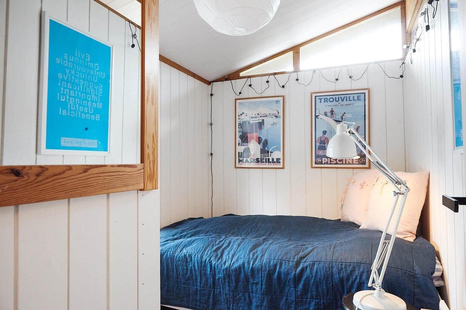 Wohnbereich mit Fernseher, Bücherregalen und Wandkunst. Holzmöbel und Küchenbereich sichtbar.