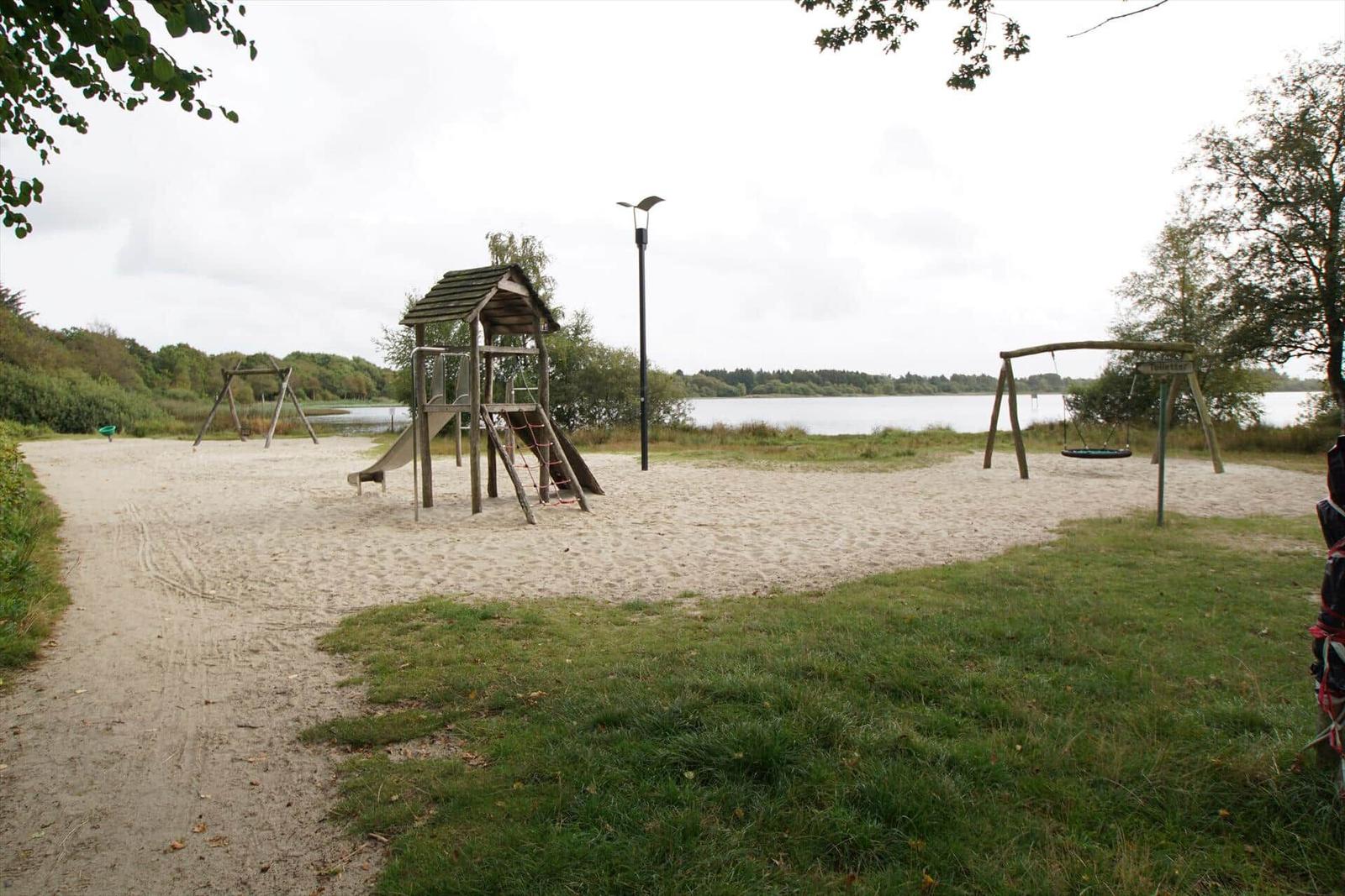 Holzschild mit Schriftzug PANDEKAGEHUSSET an Pfosten im Grün. Hintergrund mit Hecke und Zaun.