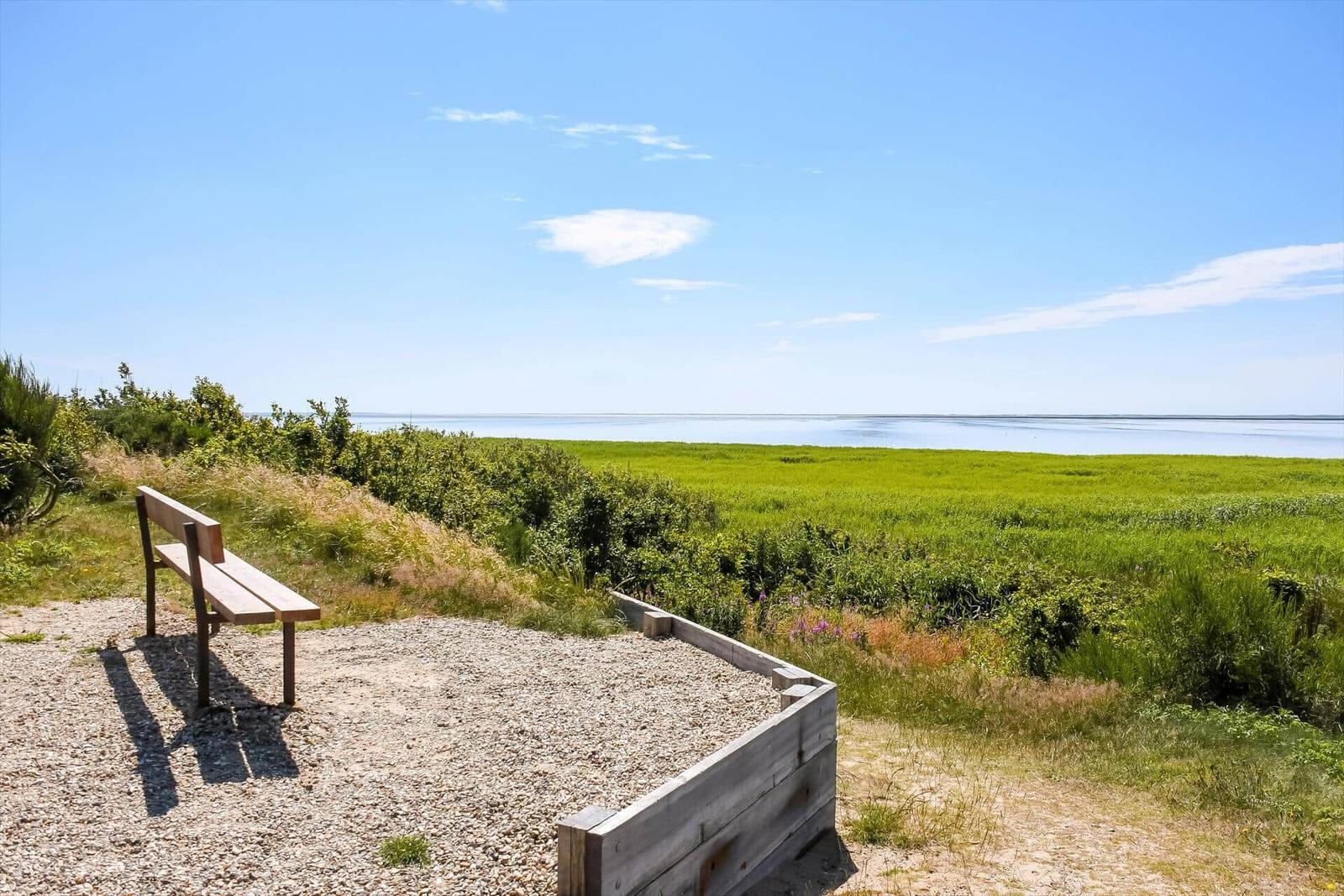 Weitläufiges Grasland mit Büschen und Blick auf das Meer unter blauem Himmel mit weißen Wolken.