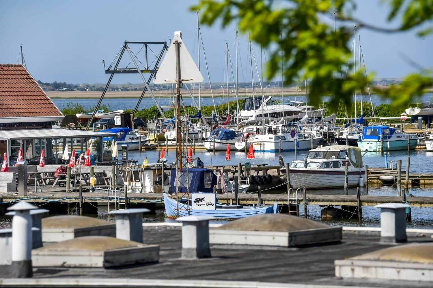 Hafen mit Booten und Steg. Im Hintergrund liegt eine Wasserfläche.
