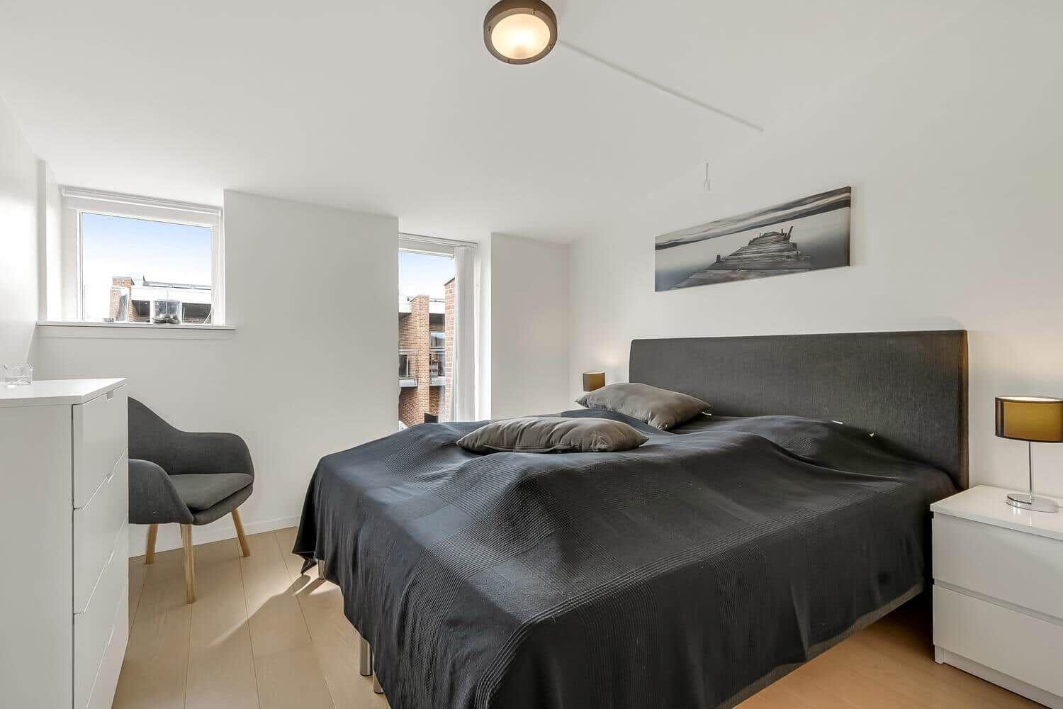 Schlafzimmer mit Doppelbett, weißen Schränken und Fenstern zum Blick auf Gebäude.
