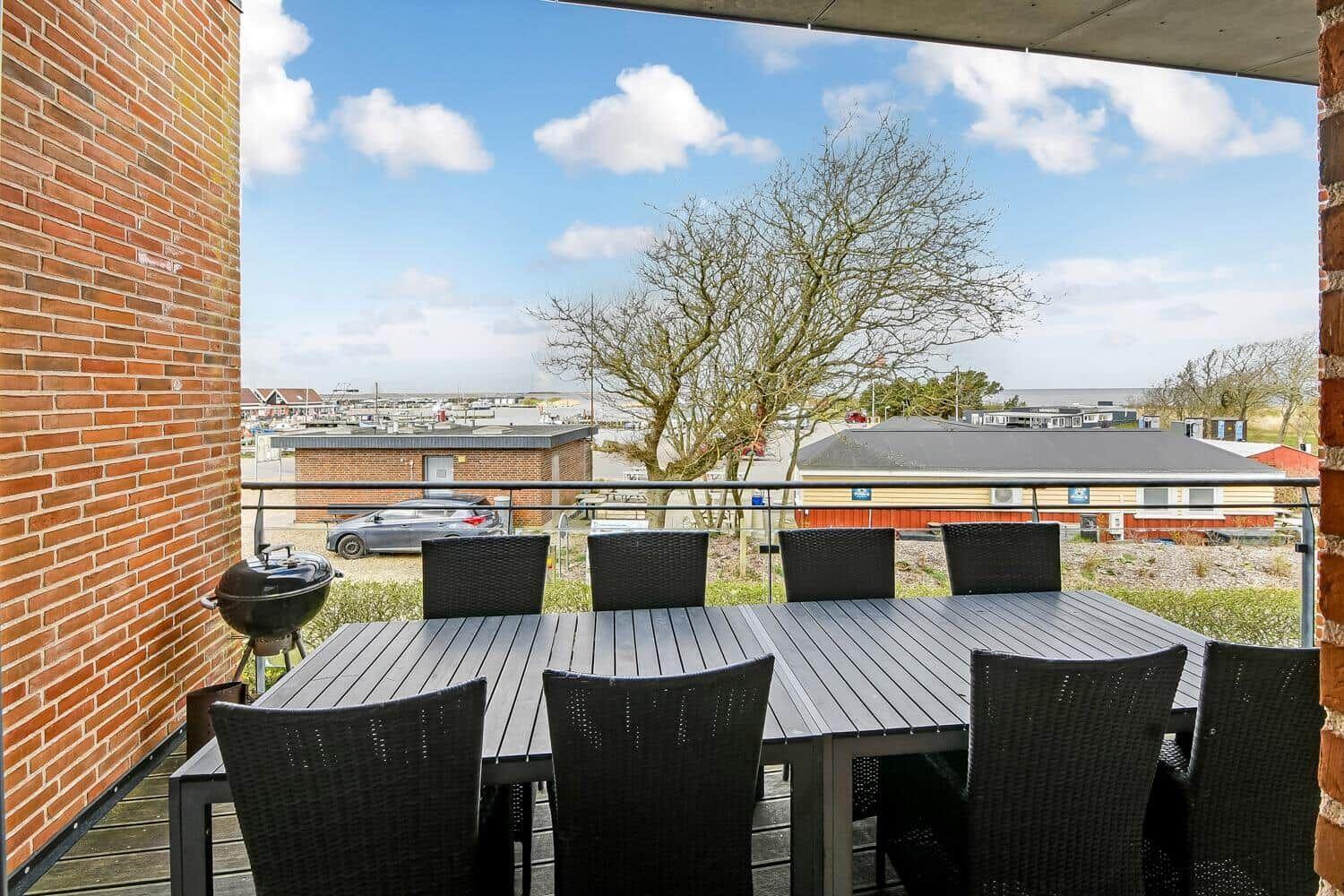 Terrasse mit Tisch, sechs Stühlen und Grill. Blick auf Gebäude und Baum.