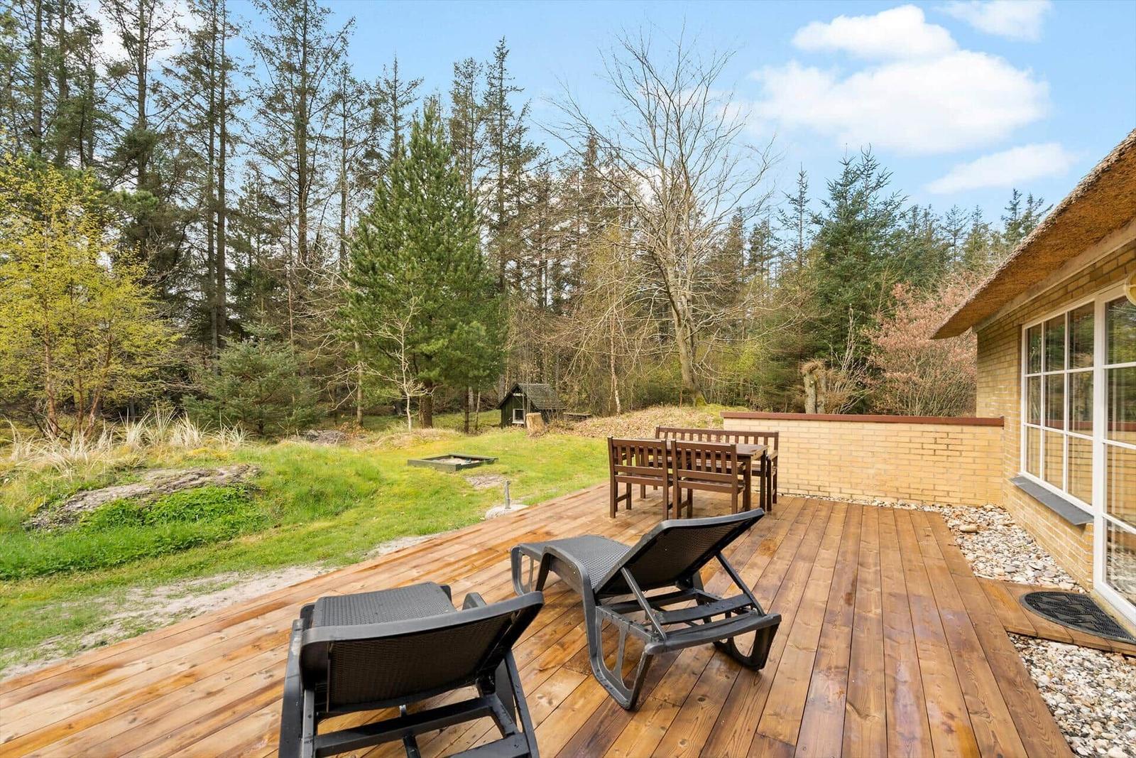 Hütte mit Strohdach, Terrasse und Picknicktisch im Wald.
