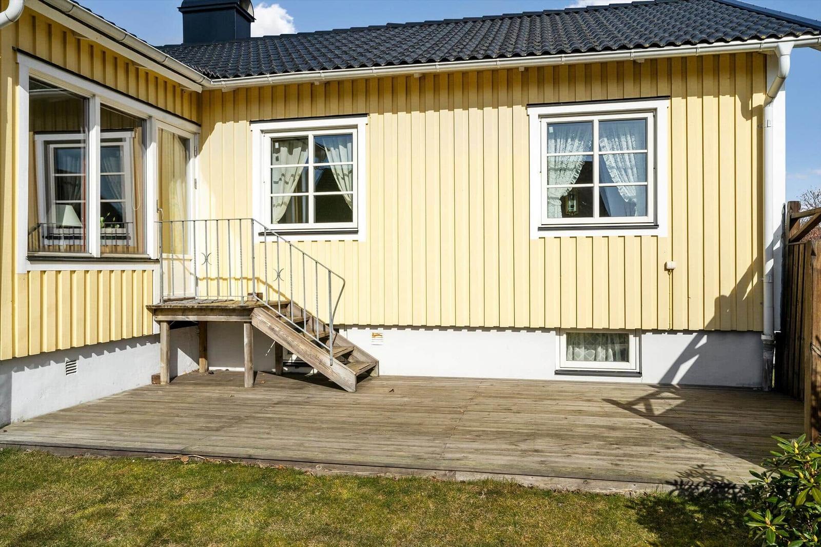 Gelbes Haus mit Holzterrasse und Treppe. Fenster mit weißen Rahmen.