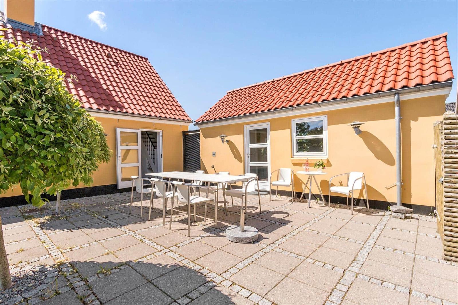 Ein gelbes Haus mit rotem Dach und weißem Gartenmöbel auf dem Hof.