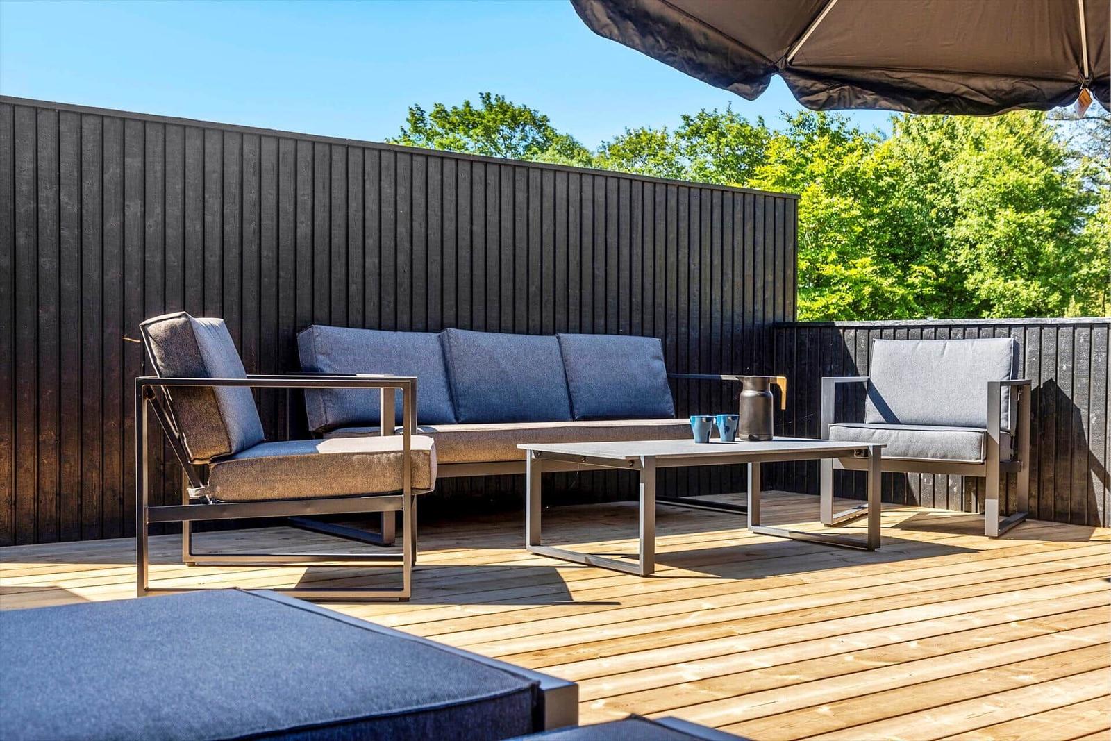 Terrasse mit Sitzgruppe, Tisch und Sonnenschutz. Holzdecke und dunkle Wand.