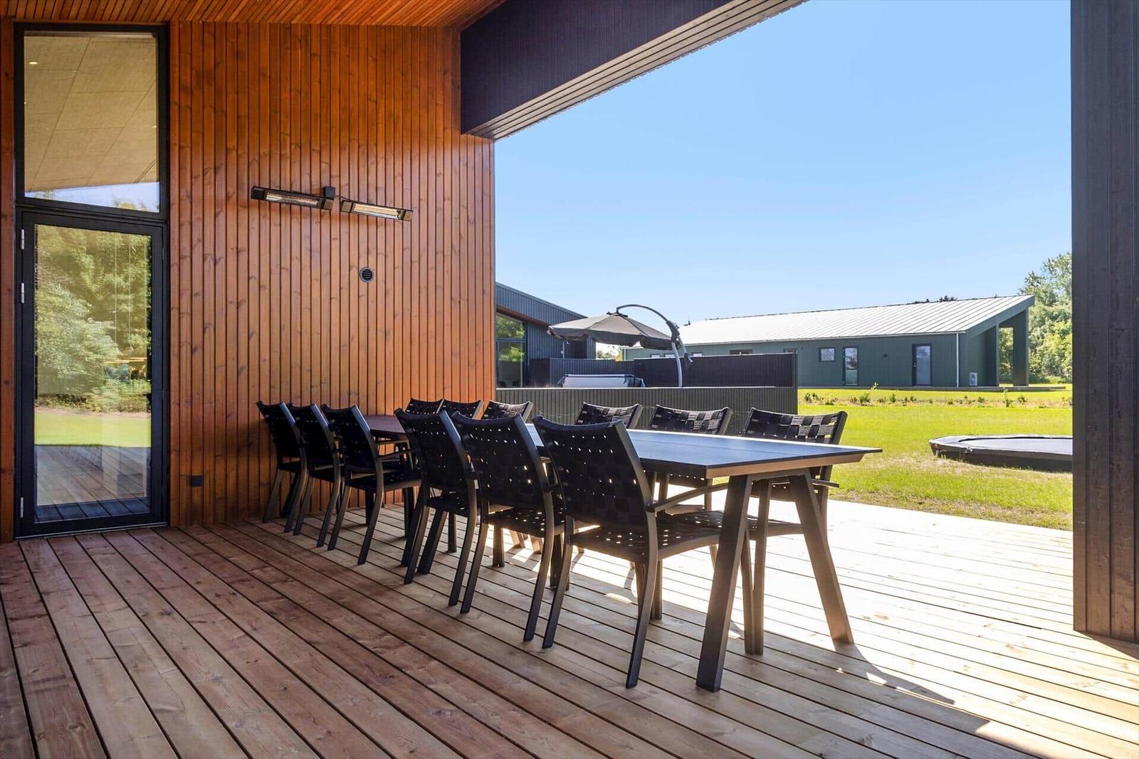 Terrasse mit großer Tischgruppe und Blick auf Garten und Trampolin.