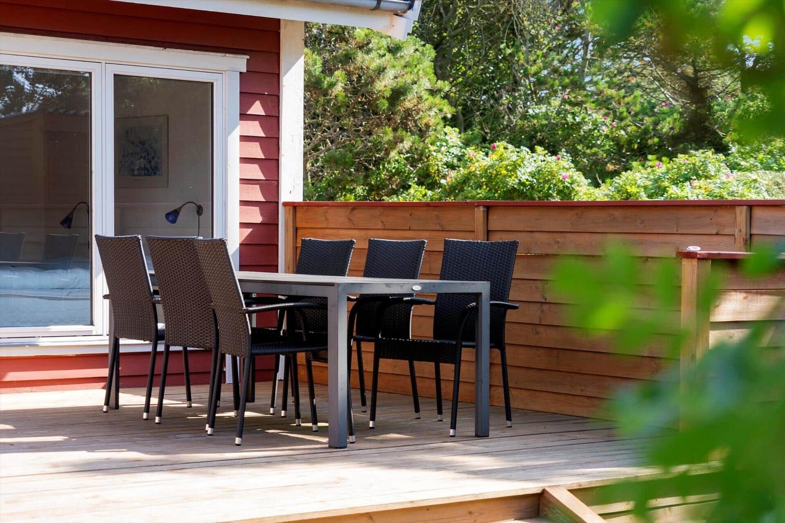 Terrasse mit Tisch und Stühlen vor einem roten Haus mit Holzgeländer.