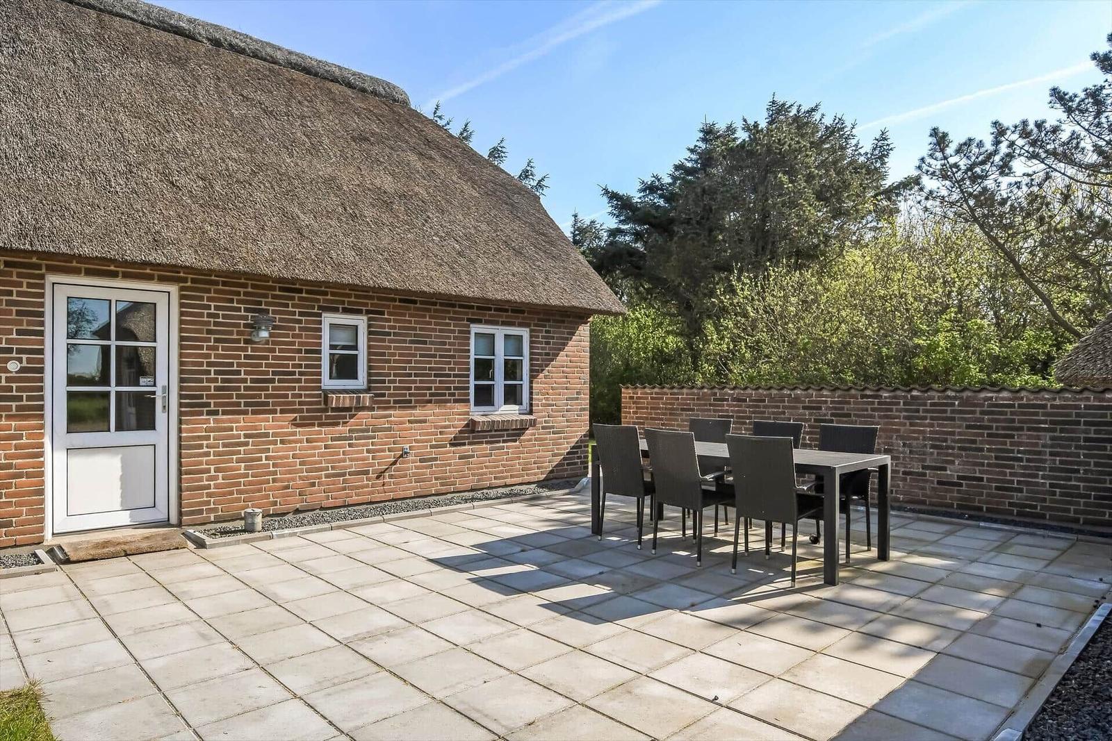 Terrasse mit Tisch und Stühlen vor einem Haus mit Strohdach.