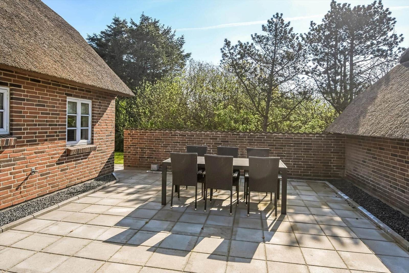 Haus mit Strohdach, Terrasse, Garten und kleinem Nebengebäude mit Strohdach.