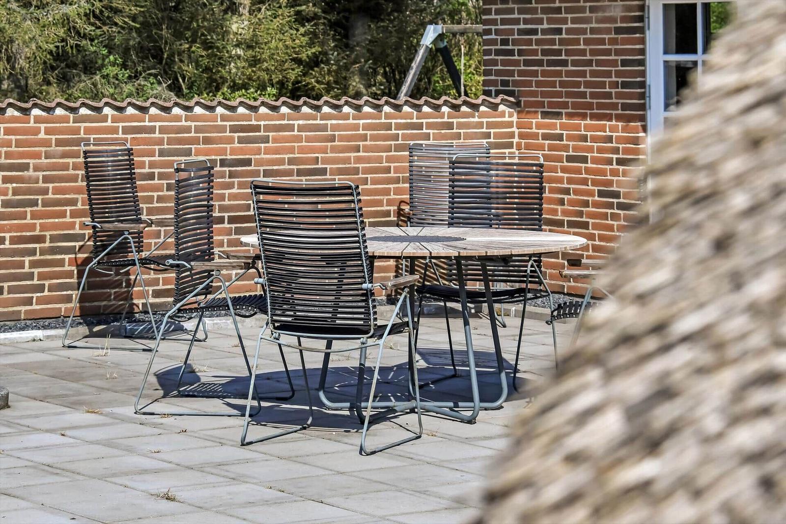 Terrasse mit Tisch und Stühlen, umgeben von Grünfläche und Ziegelmauer.