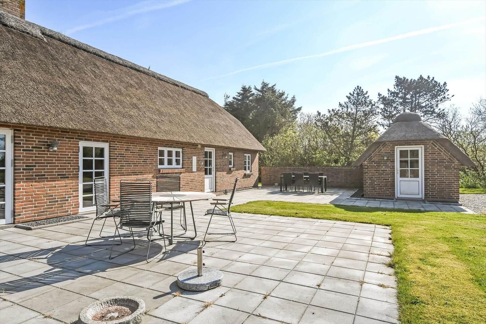 Terrasse mit Tisch und Stühlen neben einem Haus mit Strohdach und Grünfläche.