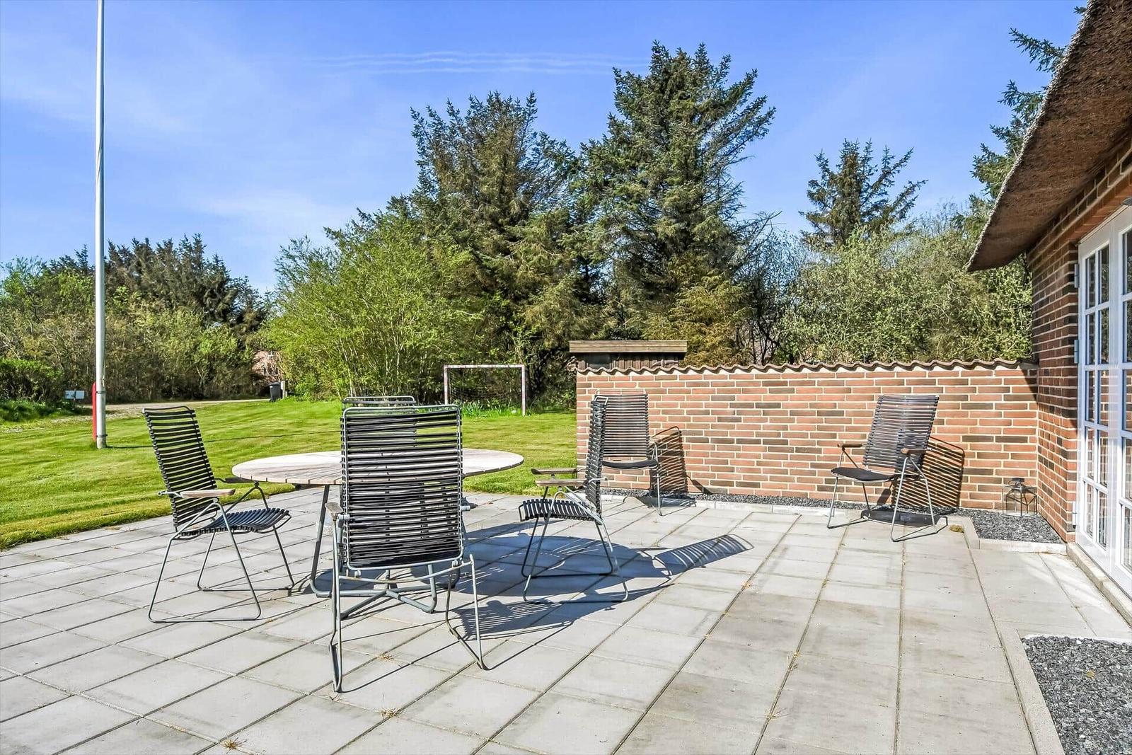 Haus mit Strohdach, Terrasse und Garten. Nebengebäude mit Tür.