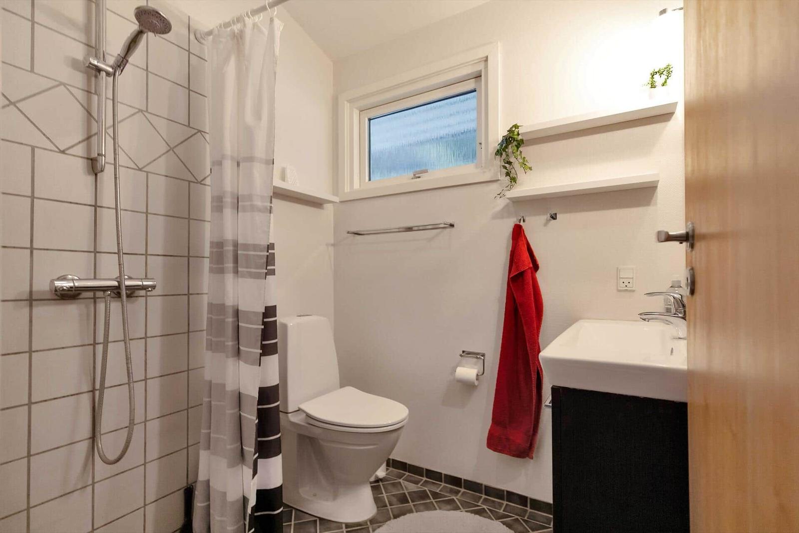 Schlafzimmer mit Bett, Kleiderhaken und Fenster. Weiße Wände und Holzboden.