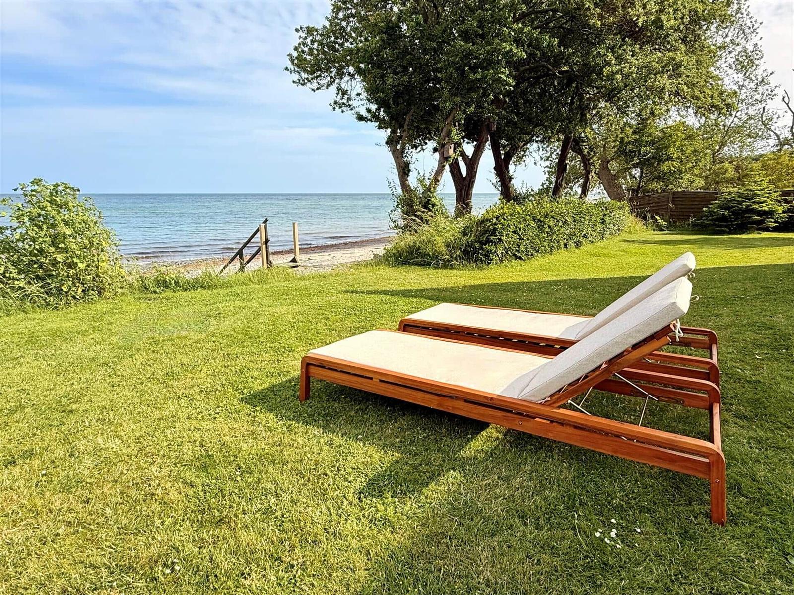 Terrasse mit zwei Tischen und Stühlen, Blick auf Meer und Bäume.