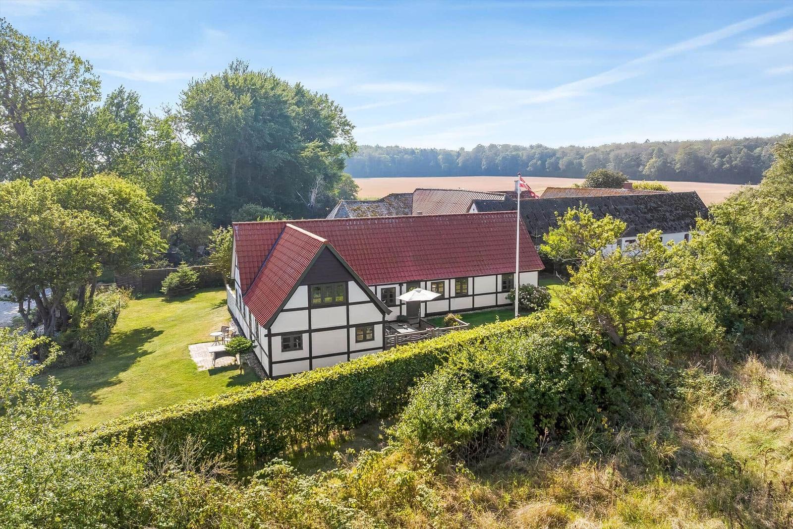 Haus mit weißer Fassade und rotem Dach, umgeben von Gras und Pflanzen.