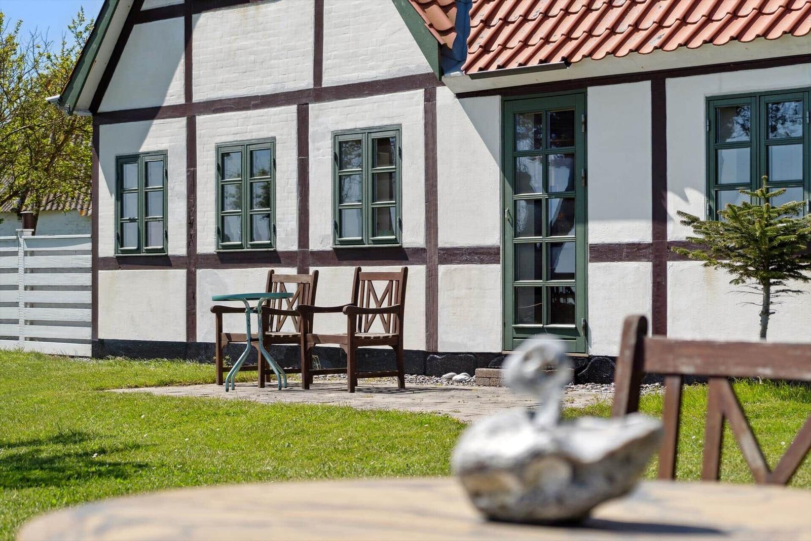 Durch ein Fenster blickt man auf einen Strand mit Grasfläche und Bäumen am Ufer.