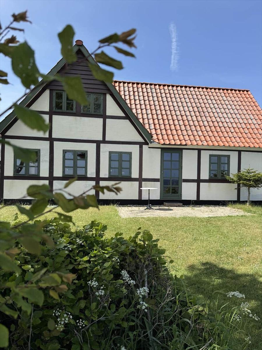 Ferienhaus mit weißem Fachwerk, rotem Dach und Garten. Daneben weht eine dänische Flagge.