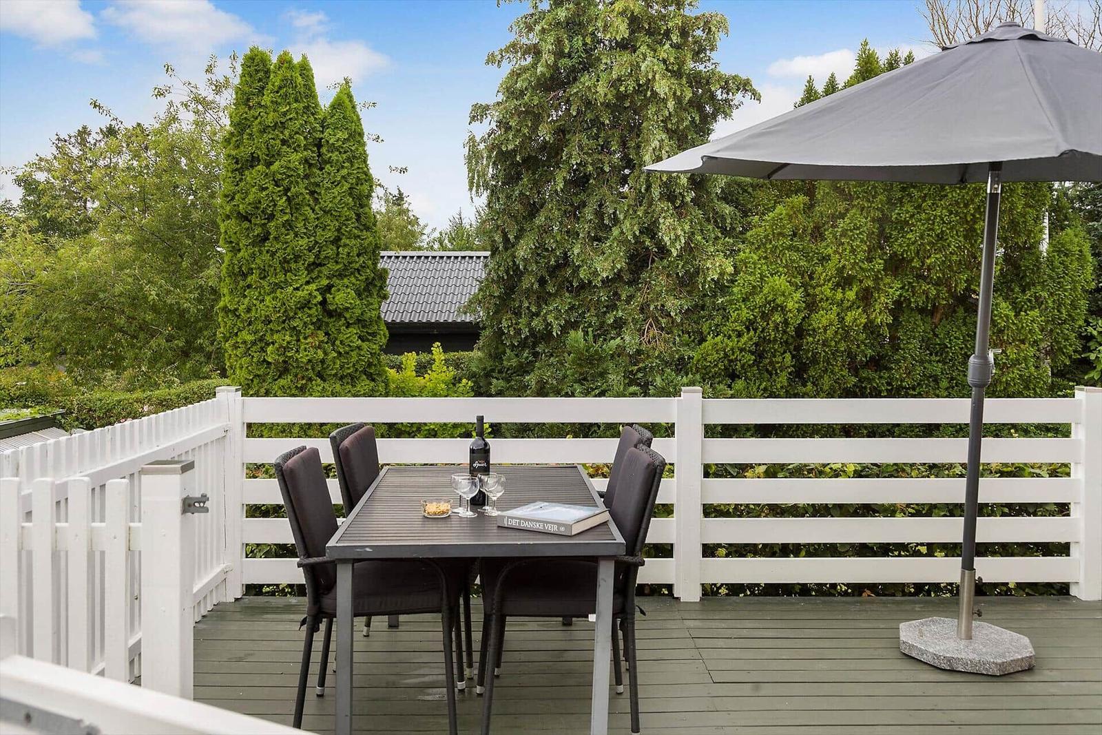 Deck with table, chairs, and umbrella. Background: house and garden.