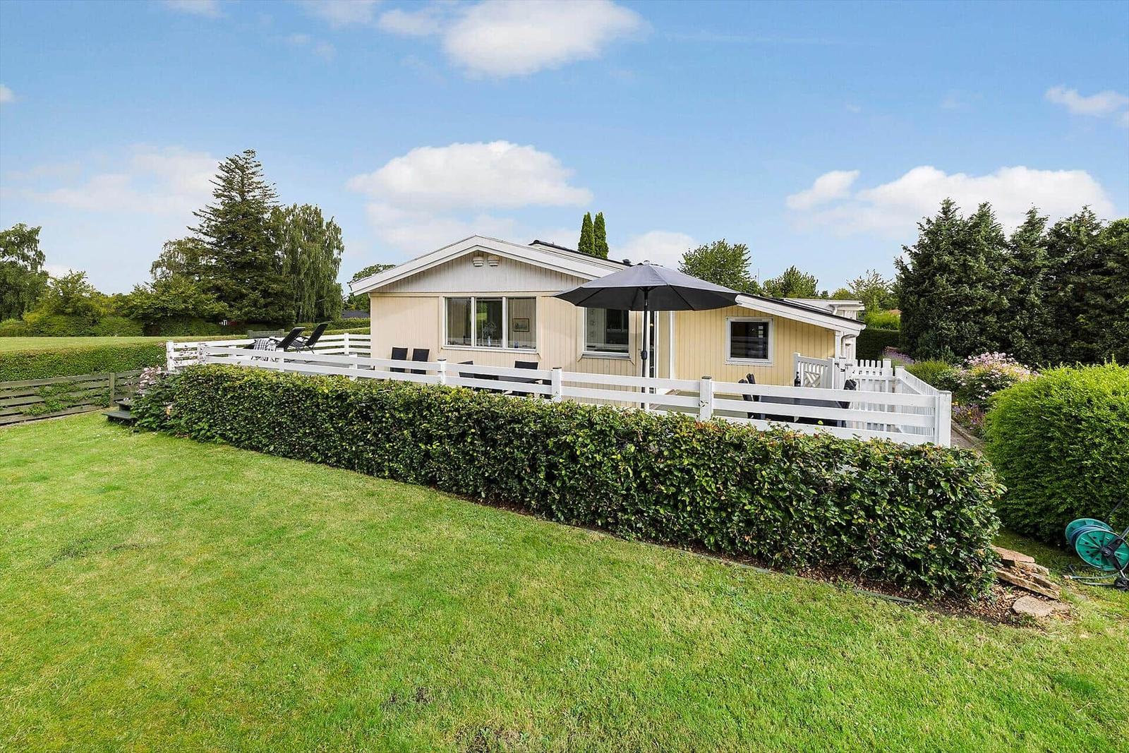 A house with garden, terrace, and barbecue area under blue sky.