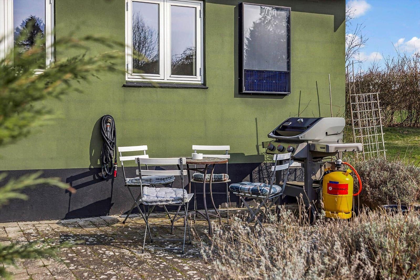 Terrasse mit Liegestuhl und Tisch. Durchgang zur Wohnung. Blick auf Wald und Nachbarhaus.