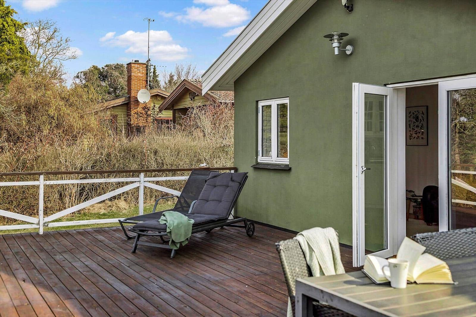 Grünes Haus mit Garten und Terrasse unter blauem Himmel.