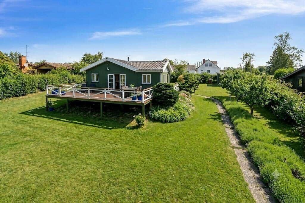 Grünes Ferienhaus mit Terrasse und Garten. Hintergrund: weitere Häuser und Bäume.