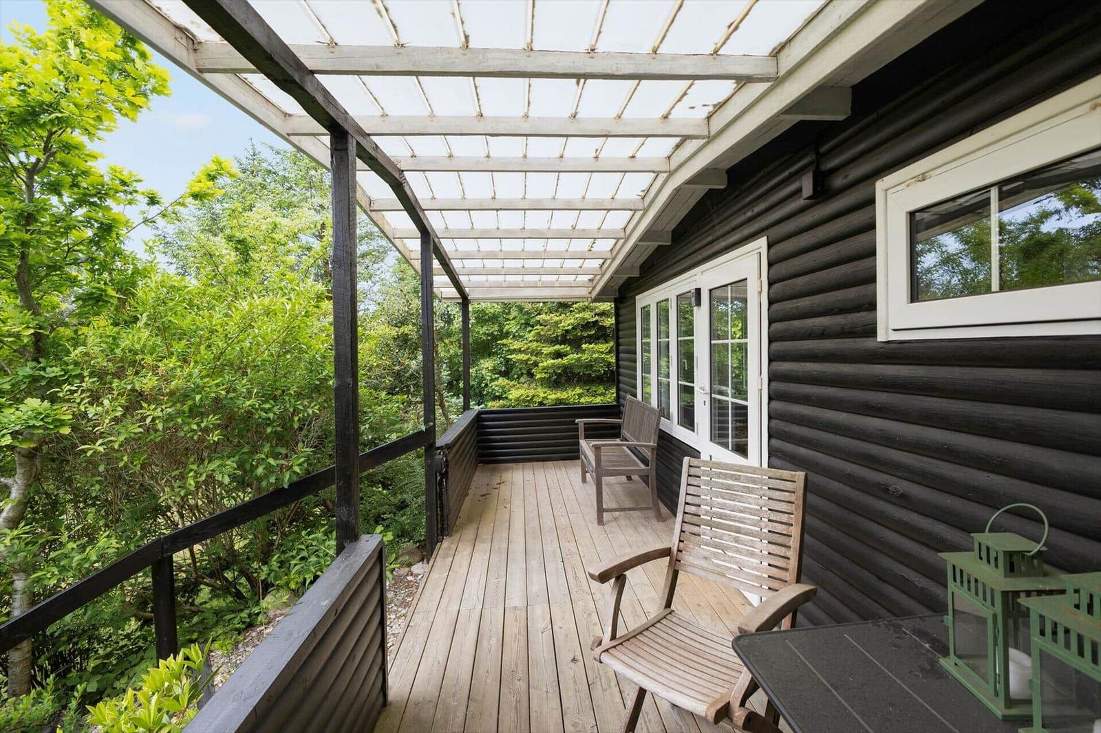 Terrasse mit Sitzbank, weiße Tür und Fenster, schwarz verputzte Wand, Glasdach, grüne Pflanzen