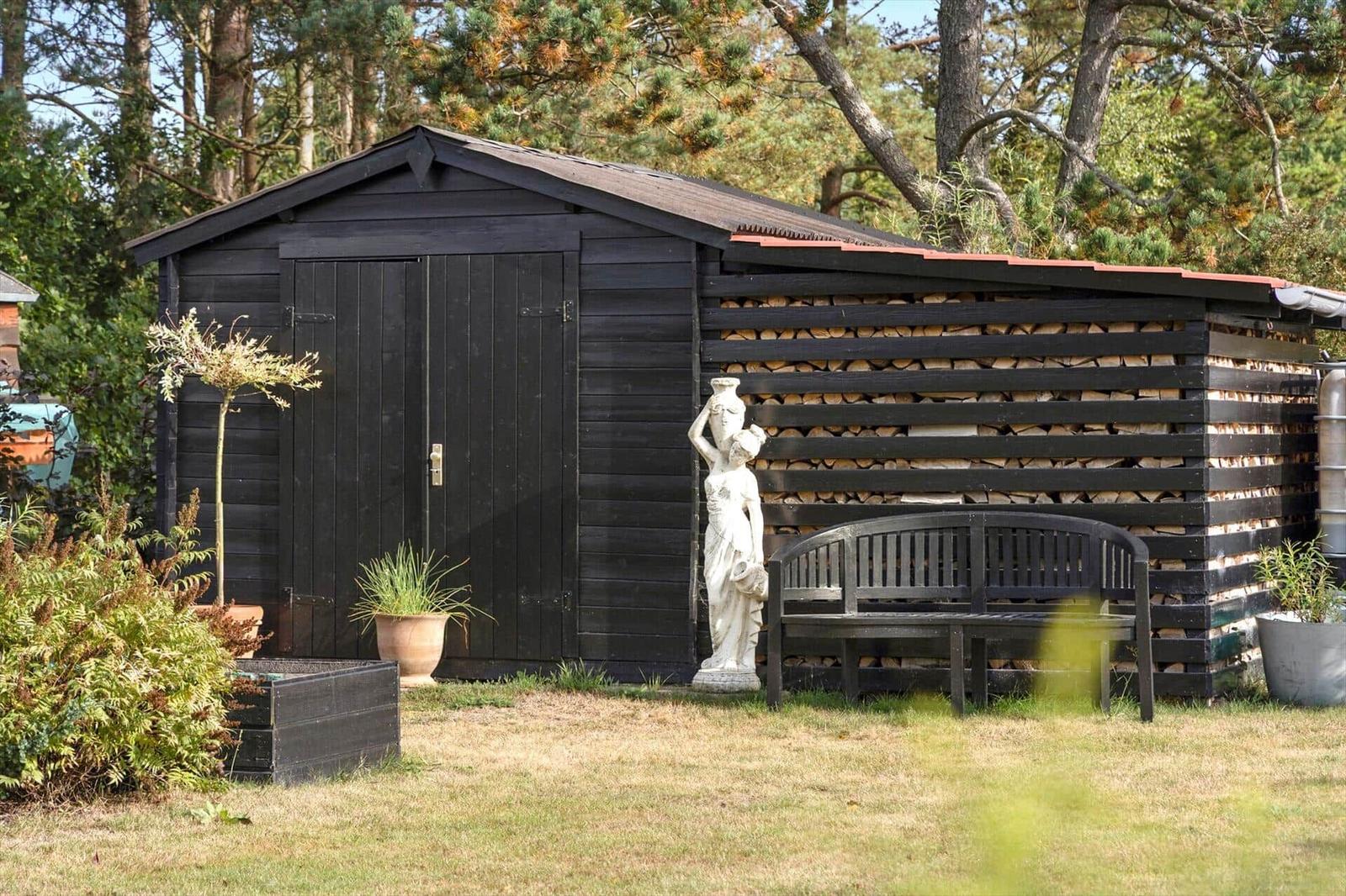 Modern wooden cabin with terrace, garden, and garage. Surrounded by trees and grass.