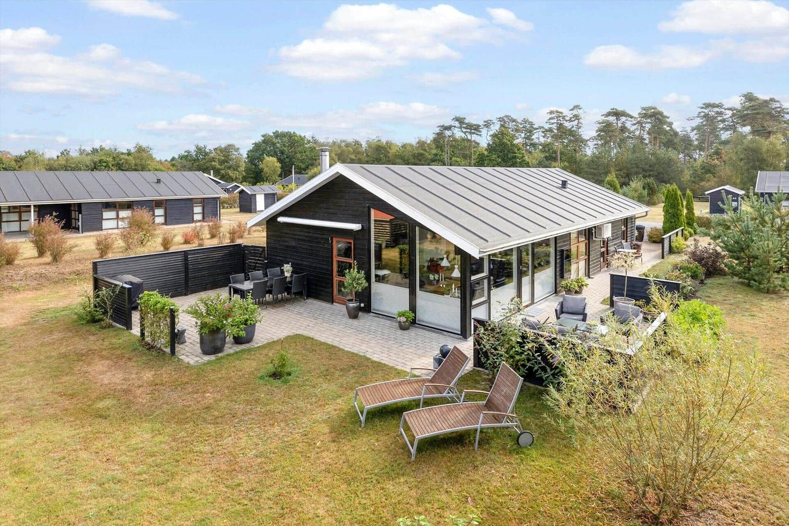 Black wooden shed with firewood stack, statue, and bench in the garden.