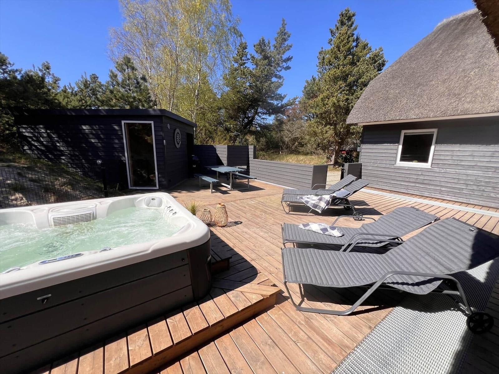 Terrasse mit Liegen, Whirlpool und Holzdecke vor einem Haus mit Schindeldach.
