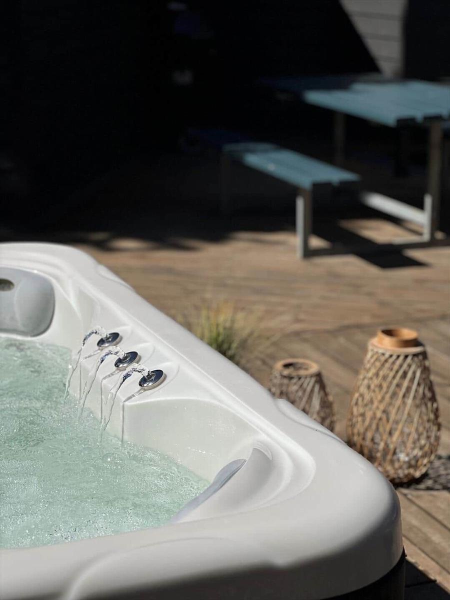 Hochwertiger Whirlpool auf Holzterrasse mit Liegestühlen und Blick auf Wald.