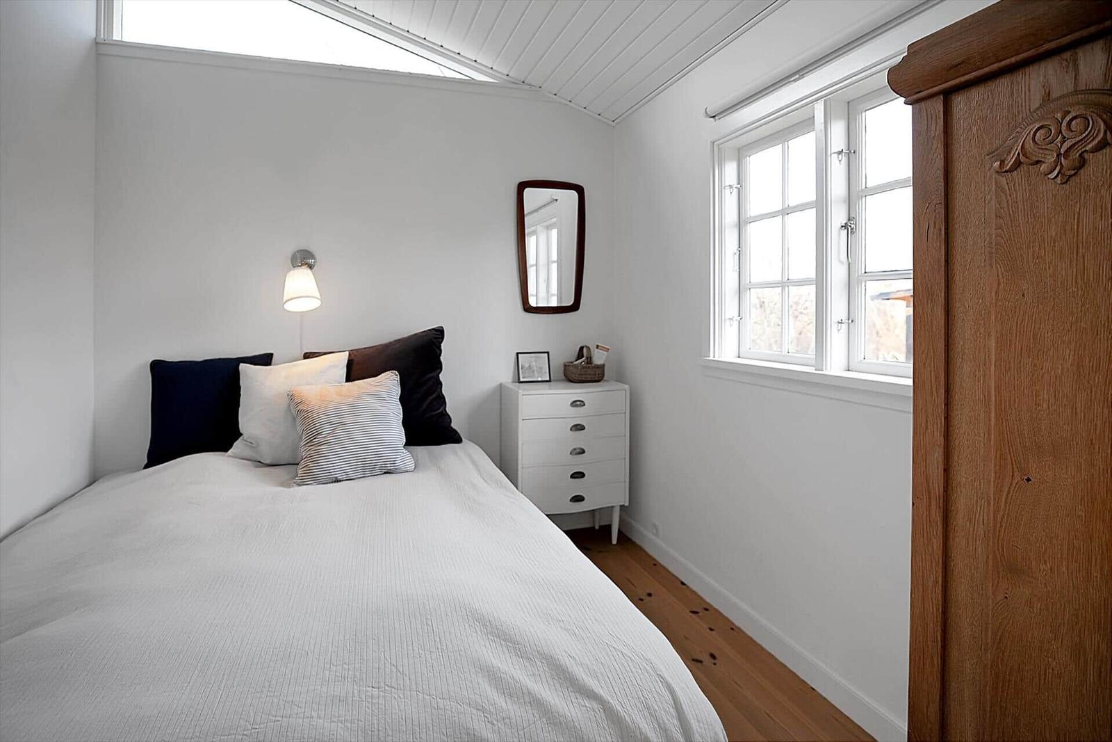 Schlafzimmer mit Bett, Wandregalen und Dachfenster. Holzboden und weiße Wände.