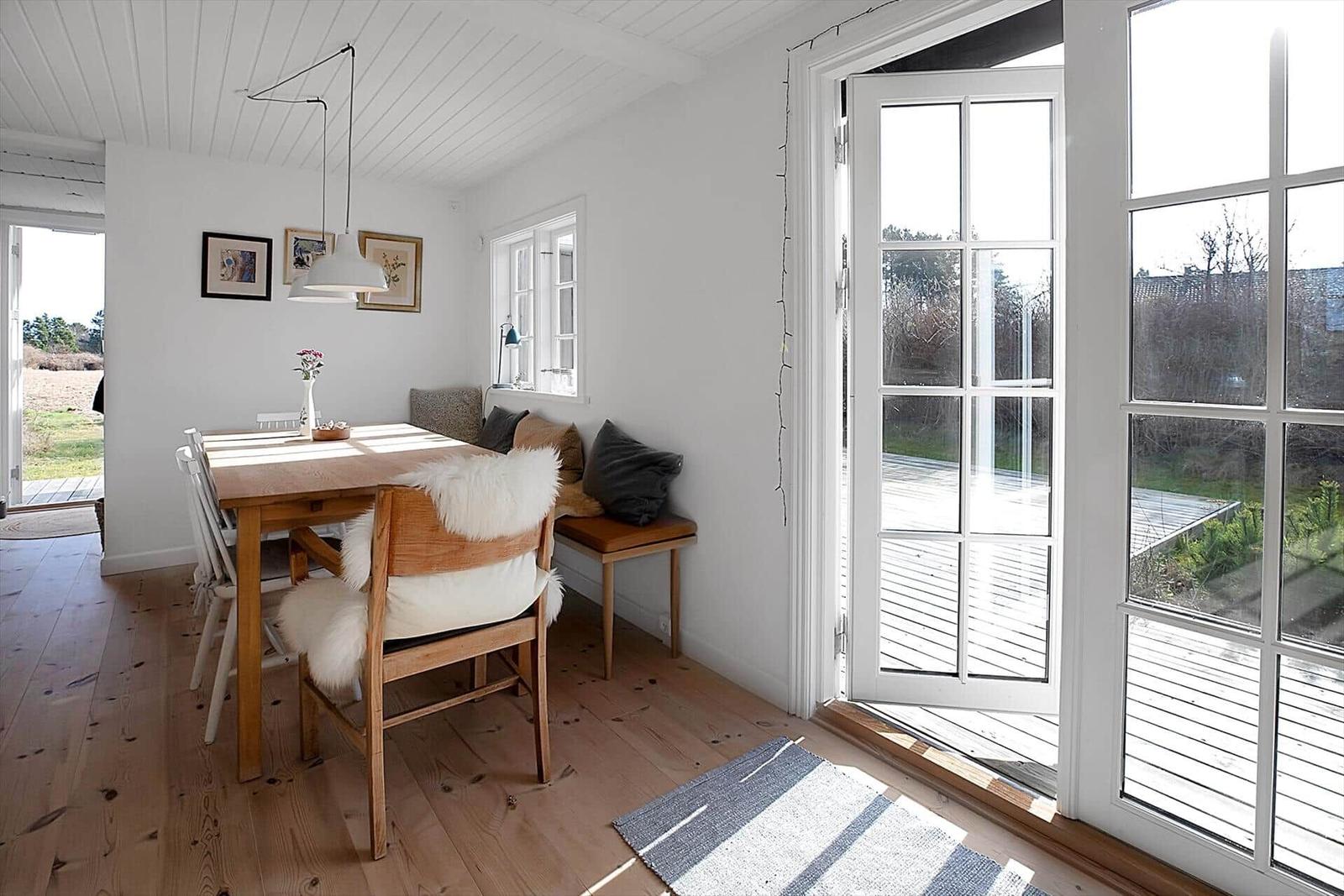 Ein Essbereich mit Holztisch, weißen Stühlen und einem Sofa mit Felldecke.