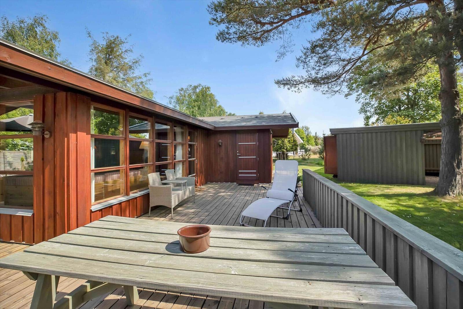 Roter Holzhaus mit Terrasse und Garten. Sichtbar: Möbel, Tisch, Sonnenschirm.