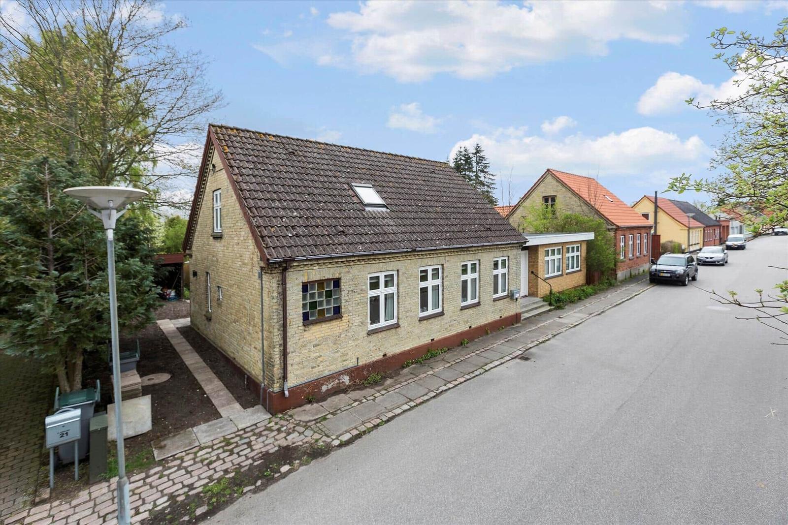 Haus mit Garten, Terrasse und Grillplatz unter blauem Himmel.