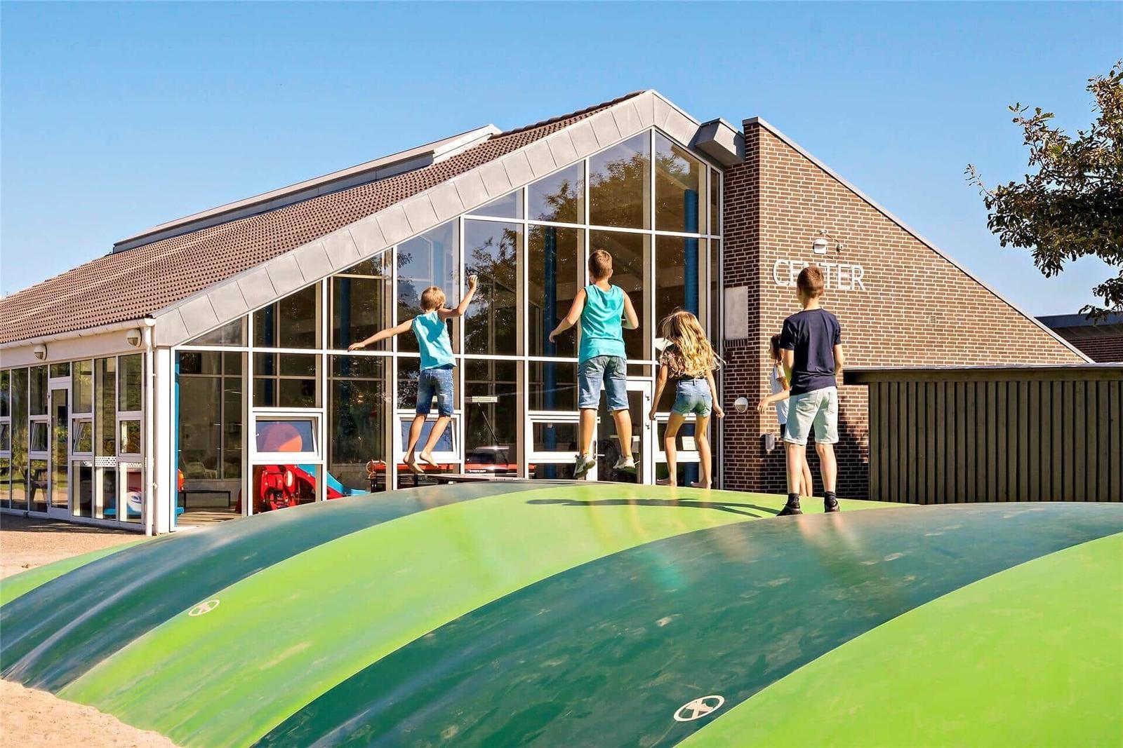 Kinder spielen auf einer grünen Rutsche vor einem Gebäude mit Glasfassade und Backsteinwand.