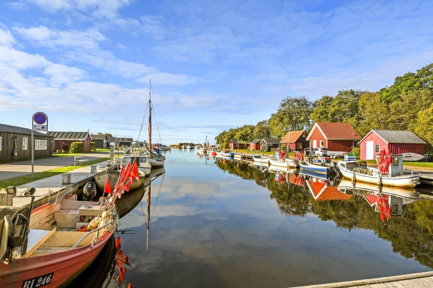 Ein Kanal mit Booten und roten Häusern spiegelt sich im Wasser.