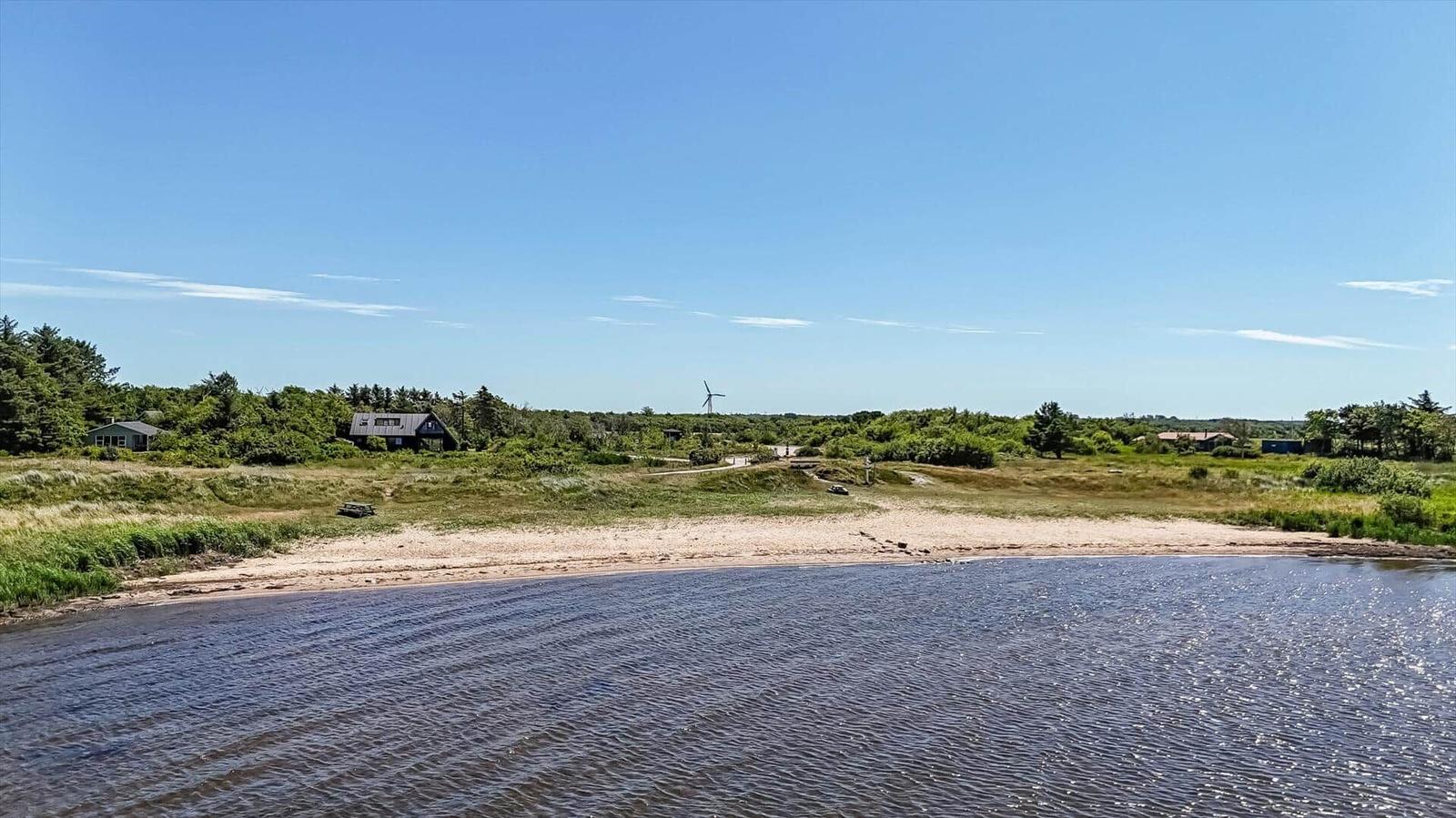 Strand mit Grünflächen und Häusern im Hintergrund unter blauem Himmel