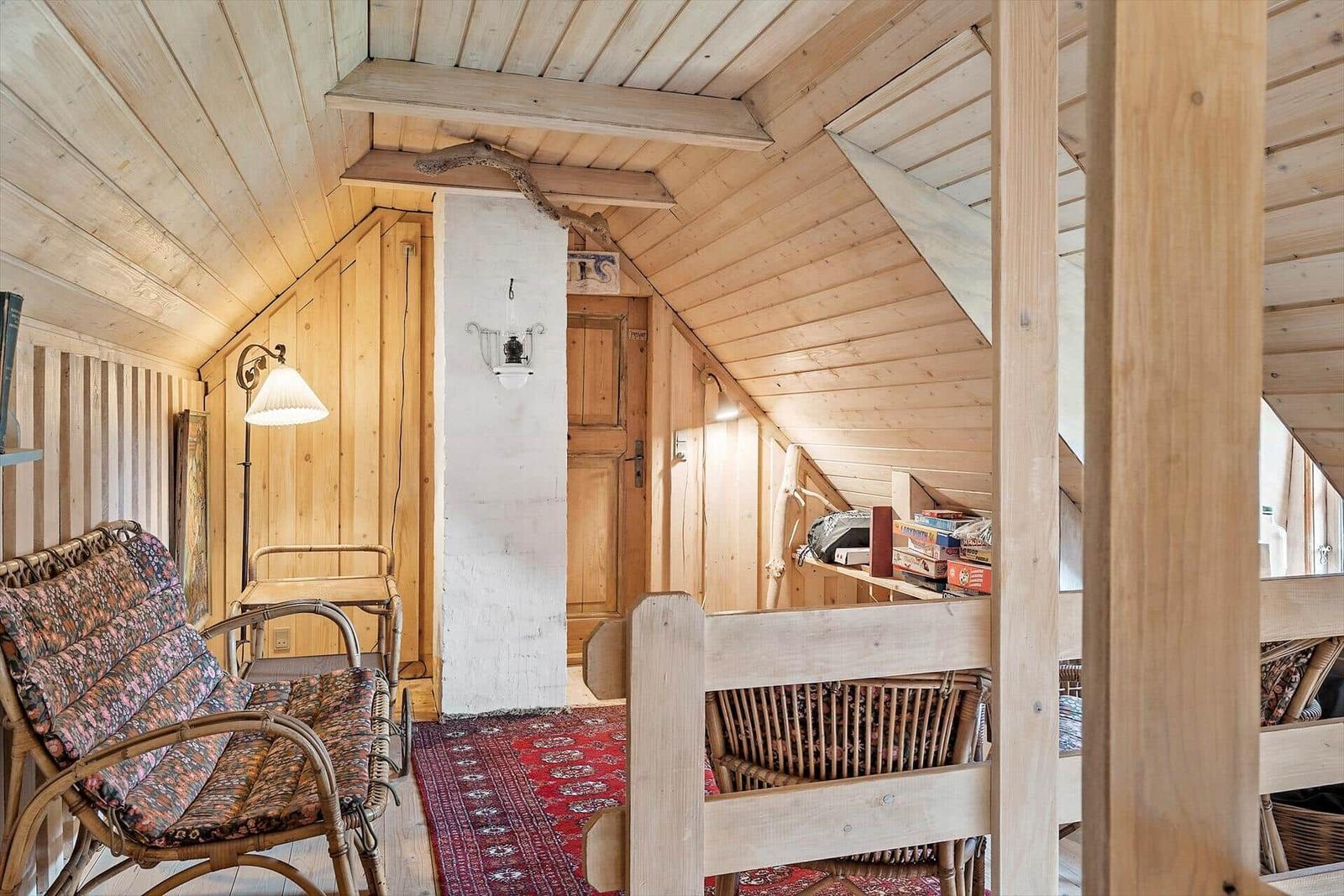 Roter Holzhaus mit Terrasse, Tisch, Stühlen und pinken Kissen. Grün hinter dem Haus.