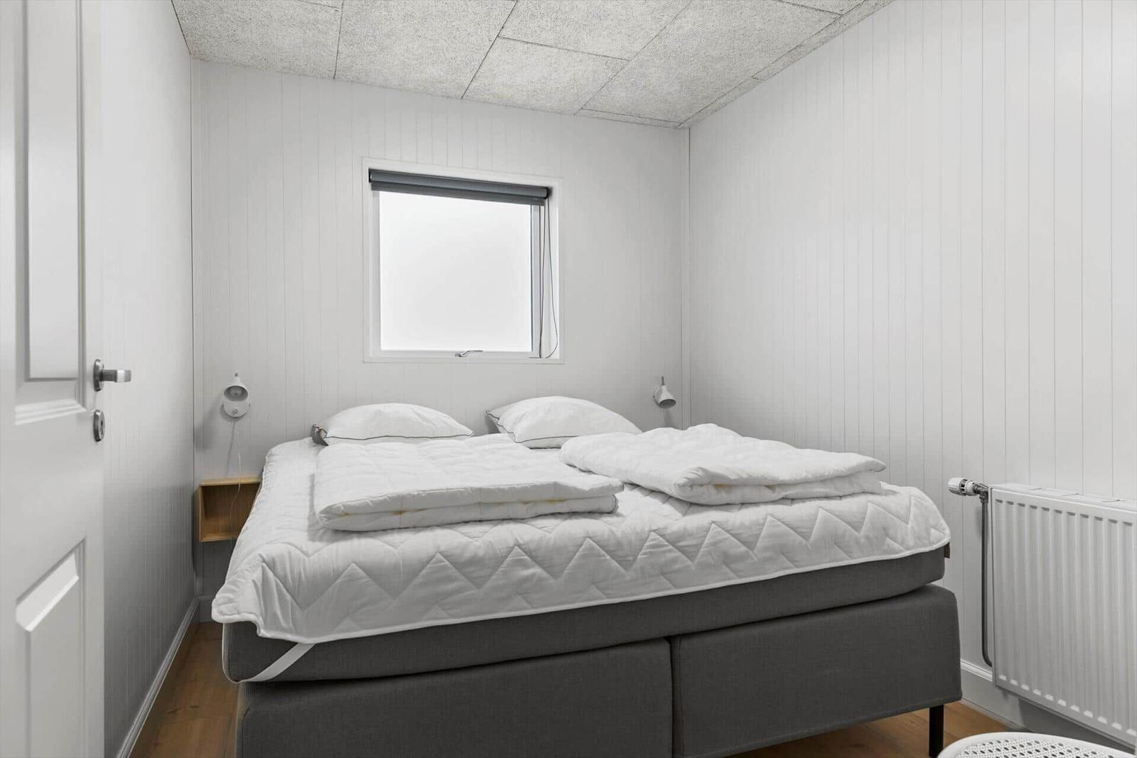 Niche with bed and green bedspread. Wall clock and plant beside. Corridor to kitchen.