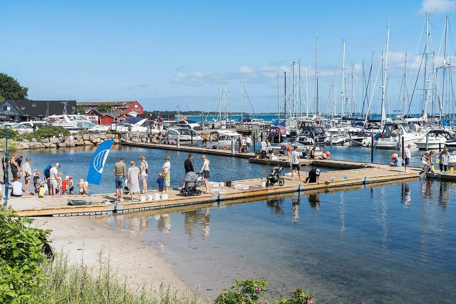 Strand mit Menschen, Segelboot und Kitesurfer im Hintergrund