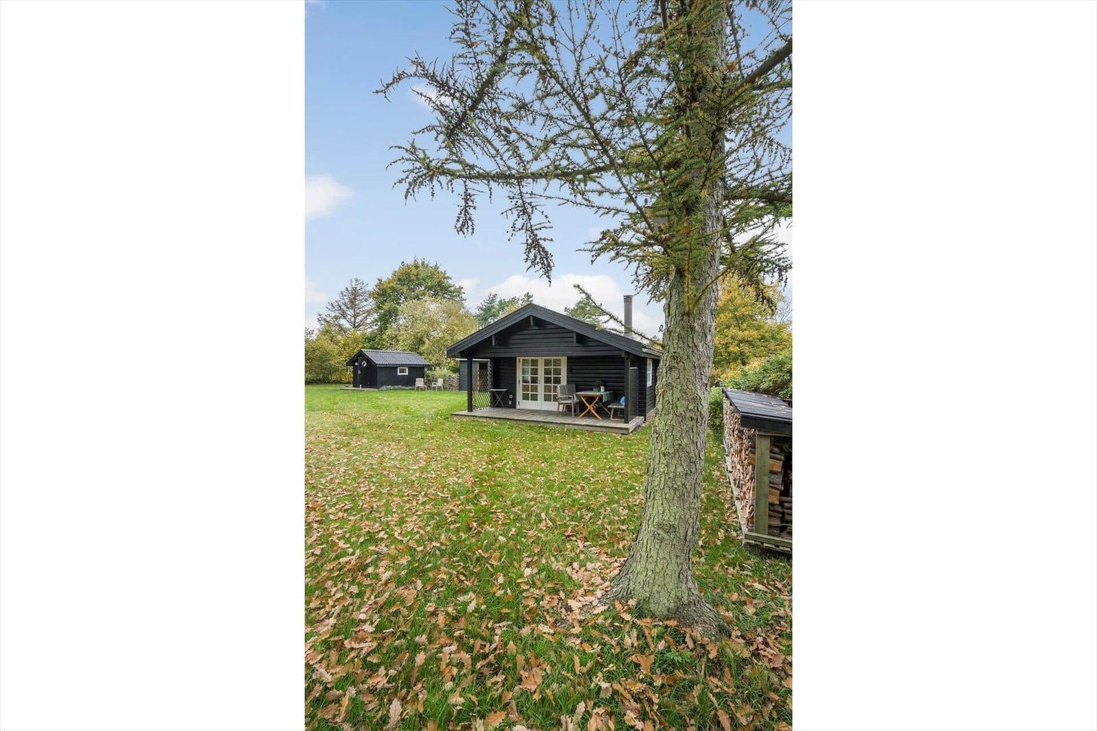 Holzhaus mit Terrasse, Tisch und Stühlen. Grünfläche und Bäume im Hintergrund.