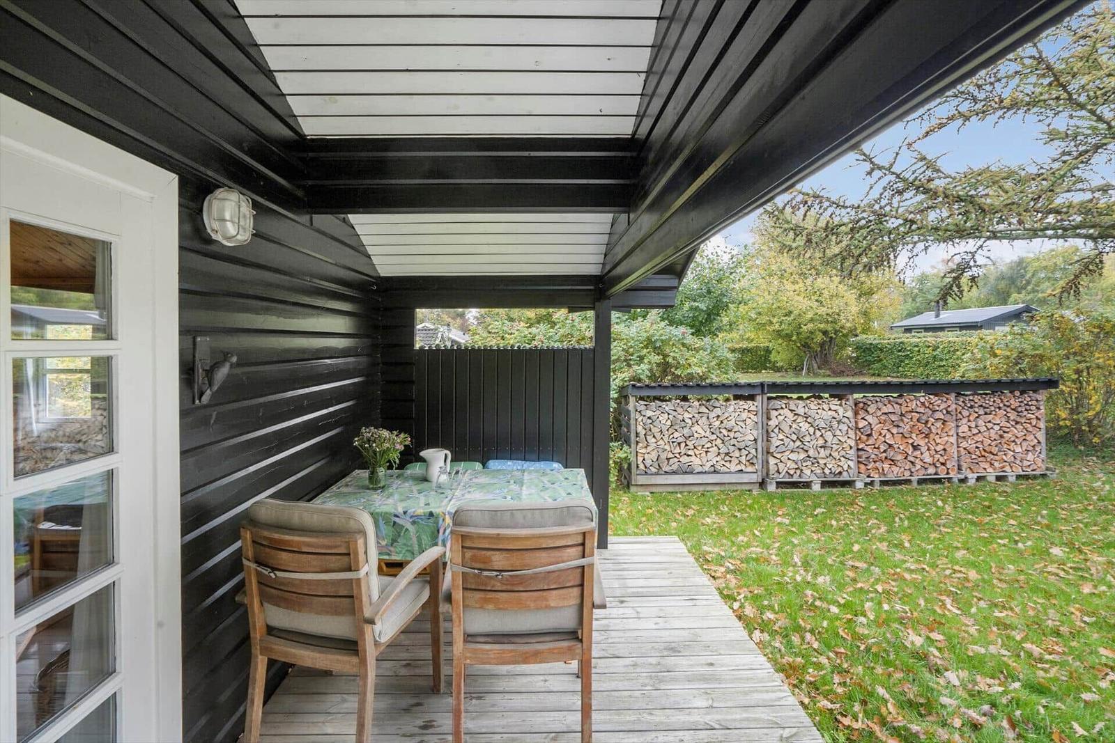 Terrasse mit Tisch, Stühlen und Tischdecke. Hintergrund: Garten und Holzhaus.